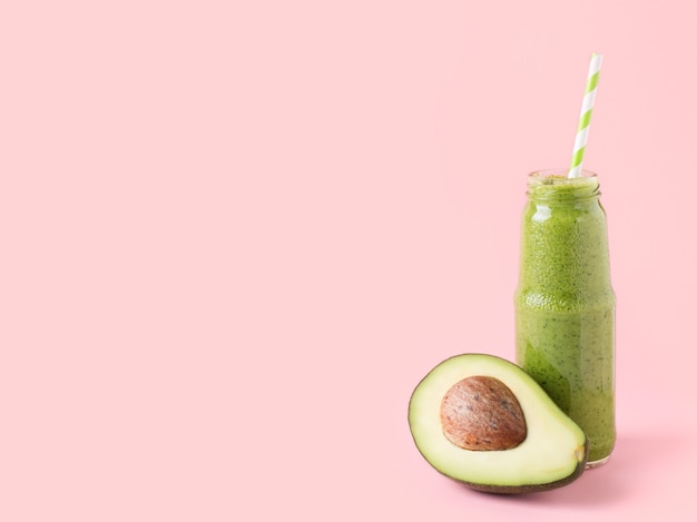 Green avocado smooothie in bottle on pink background. Creative pastel. Minimalism