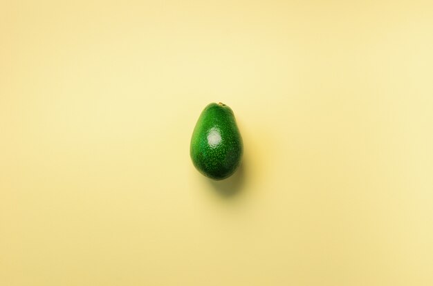 黄色の背景に緑色のアボカド。ポップアートデザイン、創造的な夏の食べ物のコンセプト。最小限の平置きスタイル。