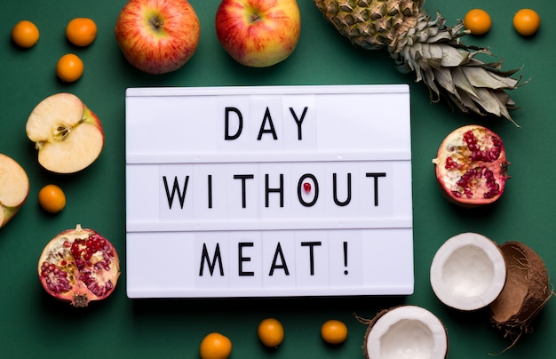 on a green background there is a lightbox with the text fruit lying next to it. international day without meat concept