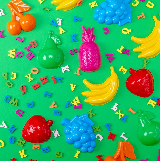 Sfondo verde con giocattoli in plastica per bambini e lettere multicolori in legno
