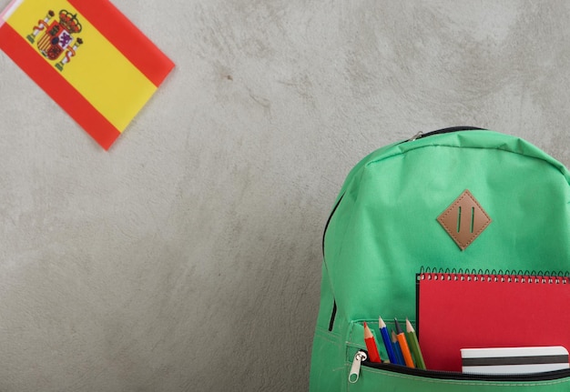 Green backpack flag of the Spain and school supplies against a cement wall