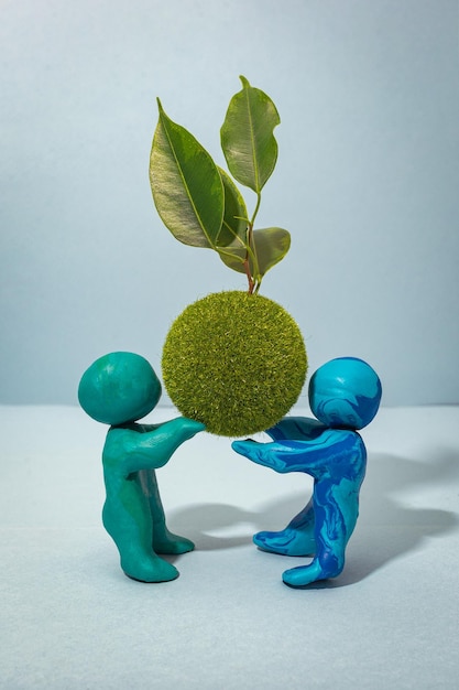 Photo the green ball with a living twig is held by two plasticine people.