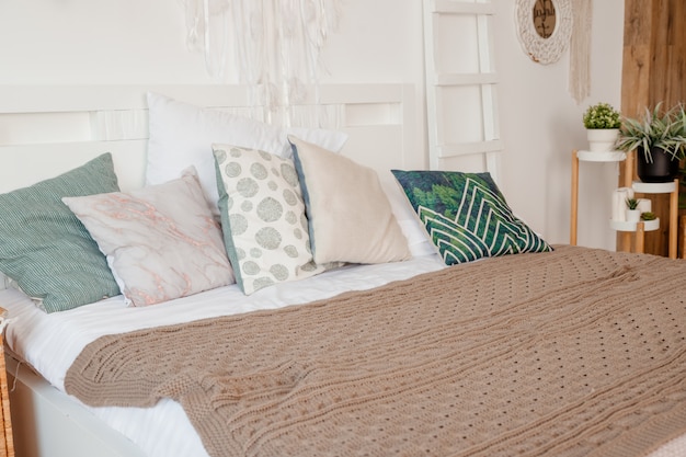 Green, beige pillow on bed in bedroom with pastel colored bedsheets on bed. stylish apartment design in lagom style.Stylish scandinavian white interior with bed, tropical plant, cozy blanket.