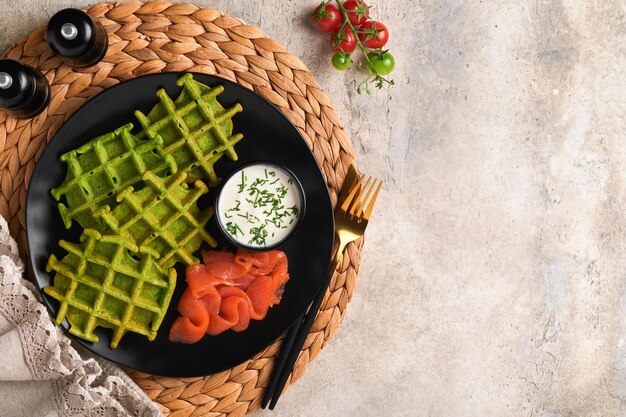 Green Belgian waffles Spinach or wild garlic or pesto waffles with red salmon and cream sauce on grey concrete table background Delicious breakfast snack brunch Top view Mock up