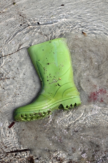 Green boots trash on beach shore pollution