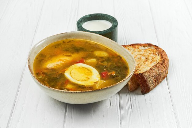 Green borscht in a plate on a white wooden background