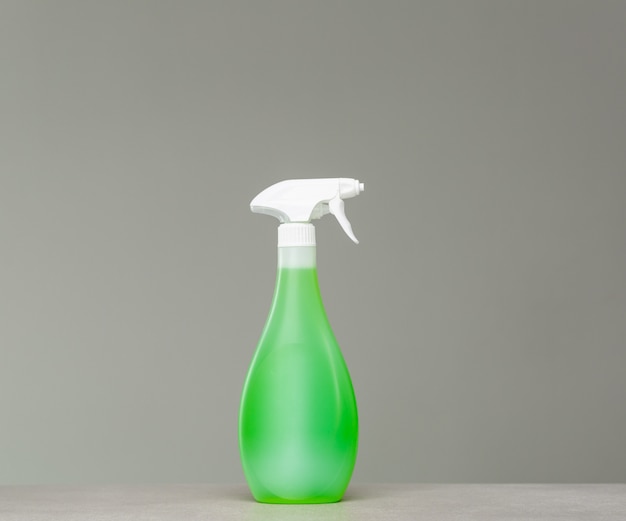 Green bottle of cleaning agent in spray on grey background.