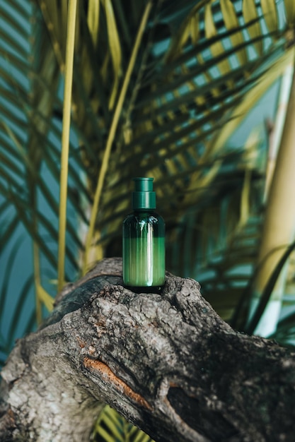 Зеленая бутылка сыворотки для лица на деревянной подставке на фоне тропических пальм Натуральная косметика для ухода за кожей