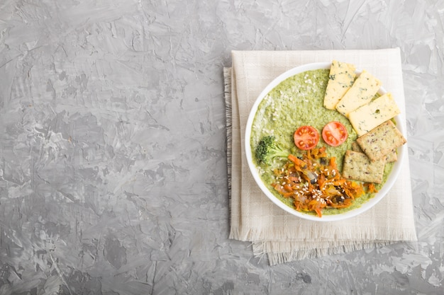 Green broccoli cream soup with crackers in white bowl, top view, copyspace.