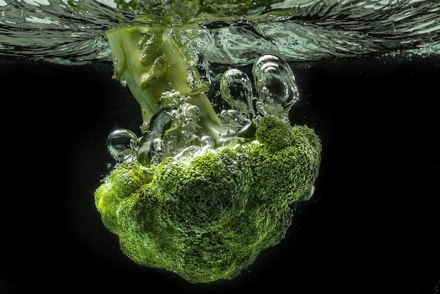 Green broccoli falling in water with splash on black with air bubbles