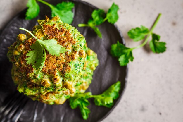 Green broccoli and pea pancakes on black plate, top view. Healthy vegan food concept.