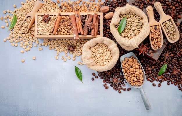 Chicchi di caffè tostati decaffeinati verdi e marroni non torrefatti e scuri in sacchi di canapa con palette montate su cemento bianco.