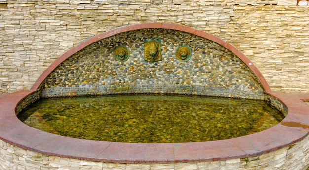 A green and brown water fountain with a stone border