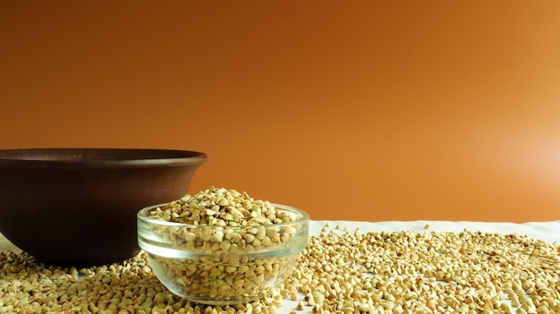 Green buckwheat in a glass transparent bowl on a brown background. healthy groats. Organic raw