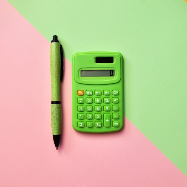 Photo green calculator and pen on a pink-green background.