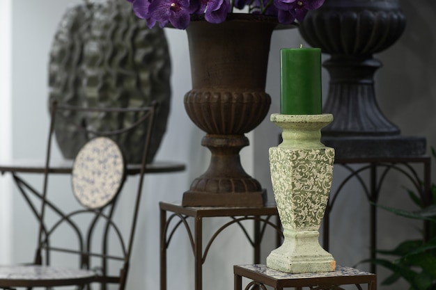 Green candle on a candlestick on the marble background of flowers and vases