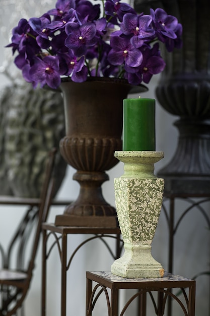 Green candle on a candlestick on the marble background of flowers and vases