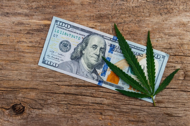 Green cannabis leaf and 100 dollar bill on the wooden table