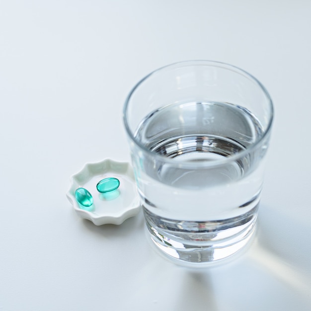 Green capsule, tablet with glass of water on white background, antibiotic