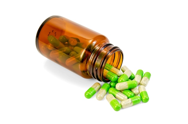 Green capsules in an open brown jar and on the table isolated