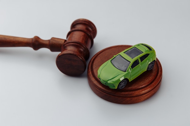 Green car and judge gavel on a white wall. Concept of selling a car by auction or accident sentence