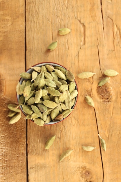 Green cardamom in ceramical bowl on wooden background closeup