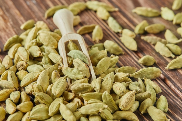 Green cardamom with wooden spatula is scattered over vintage wood background
