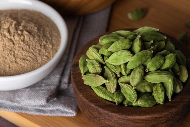 Green cardamom in wooden bowl and spoon Dry cardamom spice Cardamom seeds macro shot