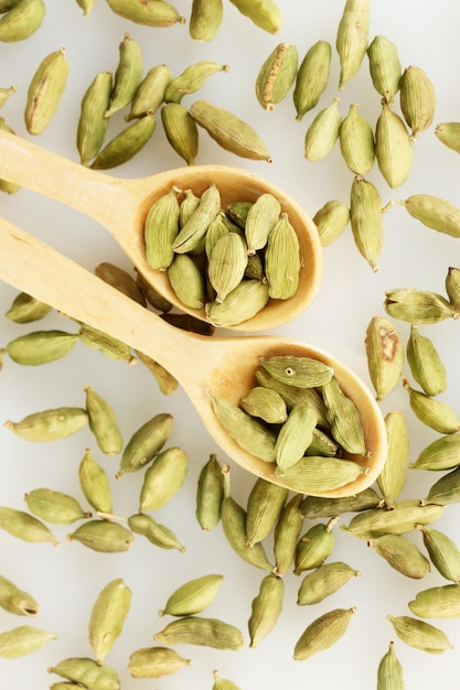 Foto cardamomo verde in cucchiai di legno su sfondo bianco