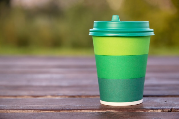 Green cardboard cup with plastic lid for coffee on wooden background or surface, mockup, close-up