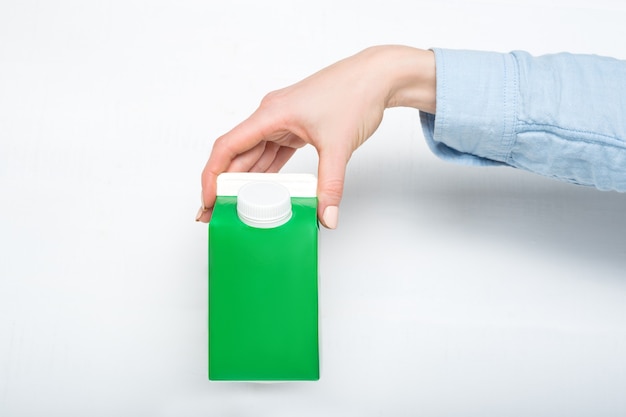 Green carton box or packaging of tetra pack with a cap in a female hand. White background