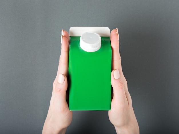 Green carton box or packaging of tetra pack with a cap in a female hands.