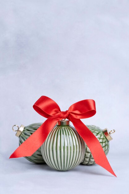 Green ceramic christmas baubles with a red bow on a light background with copy space christmas