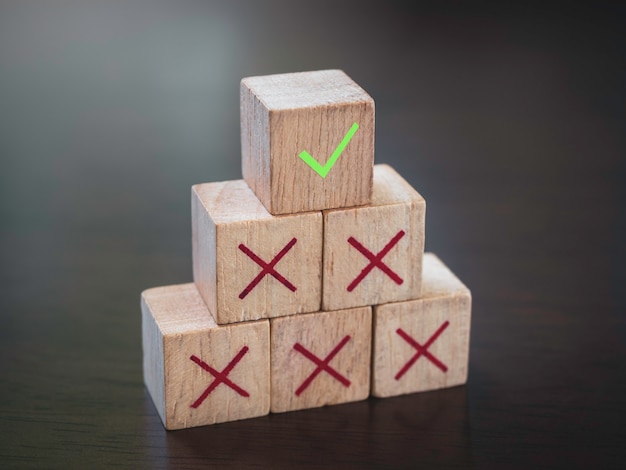 Значок зеленой галочки поверх значков красного креста на деревянных кубических блоках, ступенях пирамиды на фоне деревянного стола. Успех в бизнесе с управлением процессами, концепция устранения неполадок.
