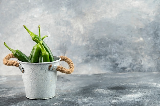 Photo green chili peppers in bucket placed on a marble table .