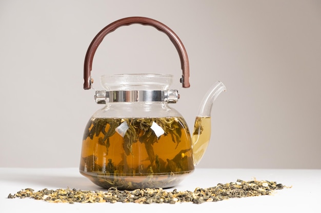 Зеленый китайский чай с апельсиновой цедрой в стеклянном чайнике на белом фоне