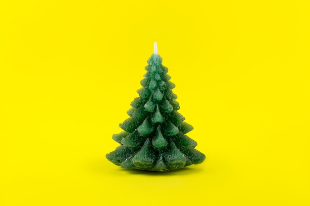 Green Christmas tree Candle on yellow background. Winter card. Holiday and celebration concept