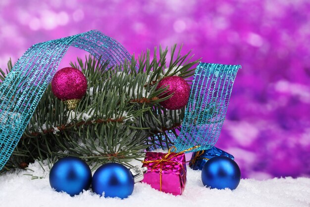 Green Christmas tree with toy and ribbon in the snow on purple