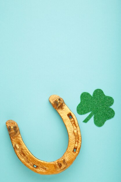 Green clovers and gold horseshoe on blue background for St. Patrick's Day Holiday. Top view.