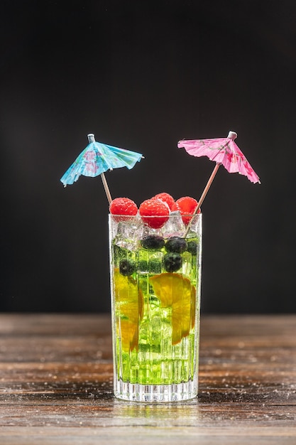 Green cocktail in a high glass decorated with orange, raspberries and blueberries