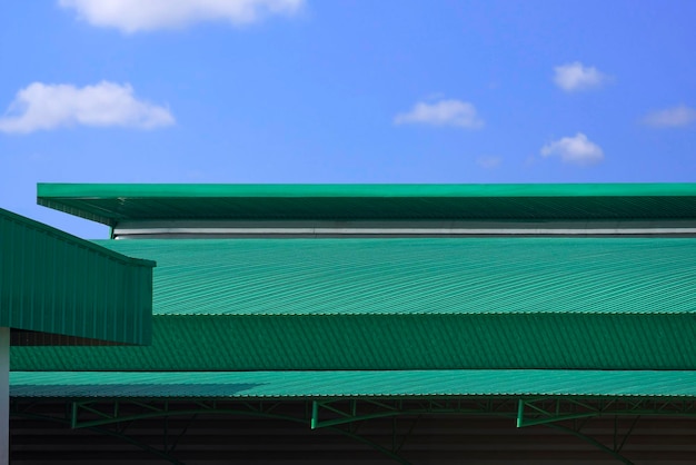 Green corrugated metal curved roof of modern factory building against blue sky background