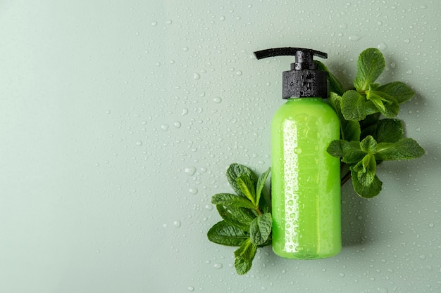 Green cosmetic bottle with dispenser, fresh mint and water drops. Organic cosmetics concept. Cosmetic container mockup with place for text. Natural skincare product.