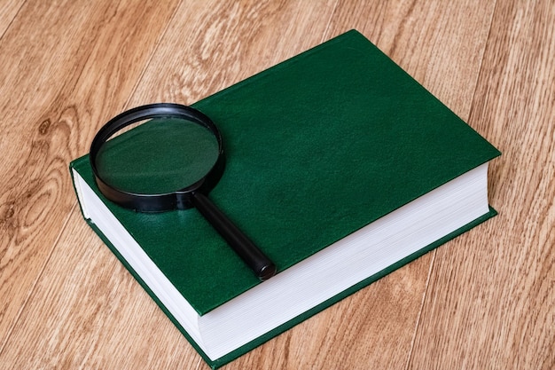 Green cover book and magnifier on wooden table