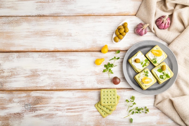 Green cracker sandwiches with cream cheese and cherry tomatoes on white wooden background top view