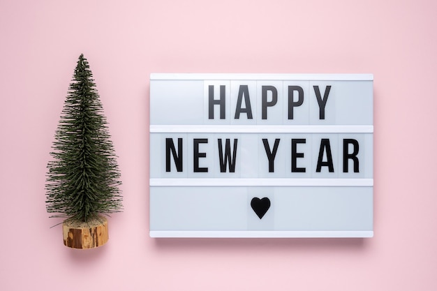 Green cristmas tree with lightbox with text HAPPY NEW YEAR on pink background