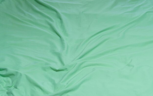 Green crumpled or wrinkled bedding sheet or blanket with pattern after guest's use taken in hotel resort room with copy space Untidy blanket background texture