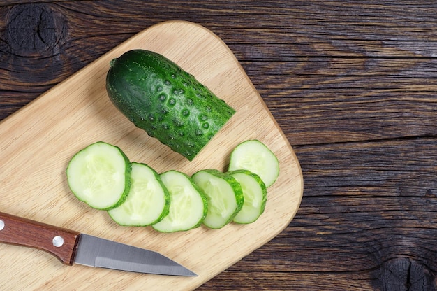 Green cucumber and slice on a cutting board on wooden background, top view