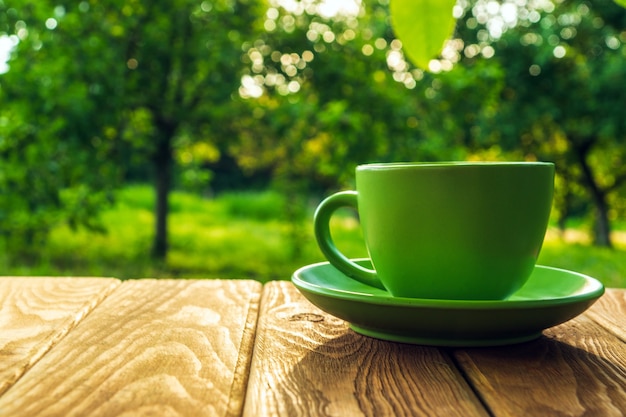 Green cup of hot coffee on a wooden table in a green garden in the morning or evening