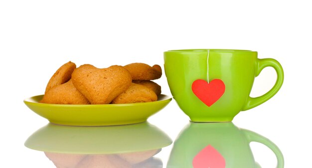 Green cup with tea bag and heart-shaped cookies on green plate isolated on white