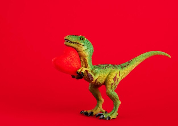 Зеленый милый динозавр с красным сердцем на красном фоне Креативная минимальная открытка на День святого Валентина